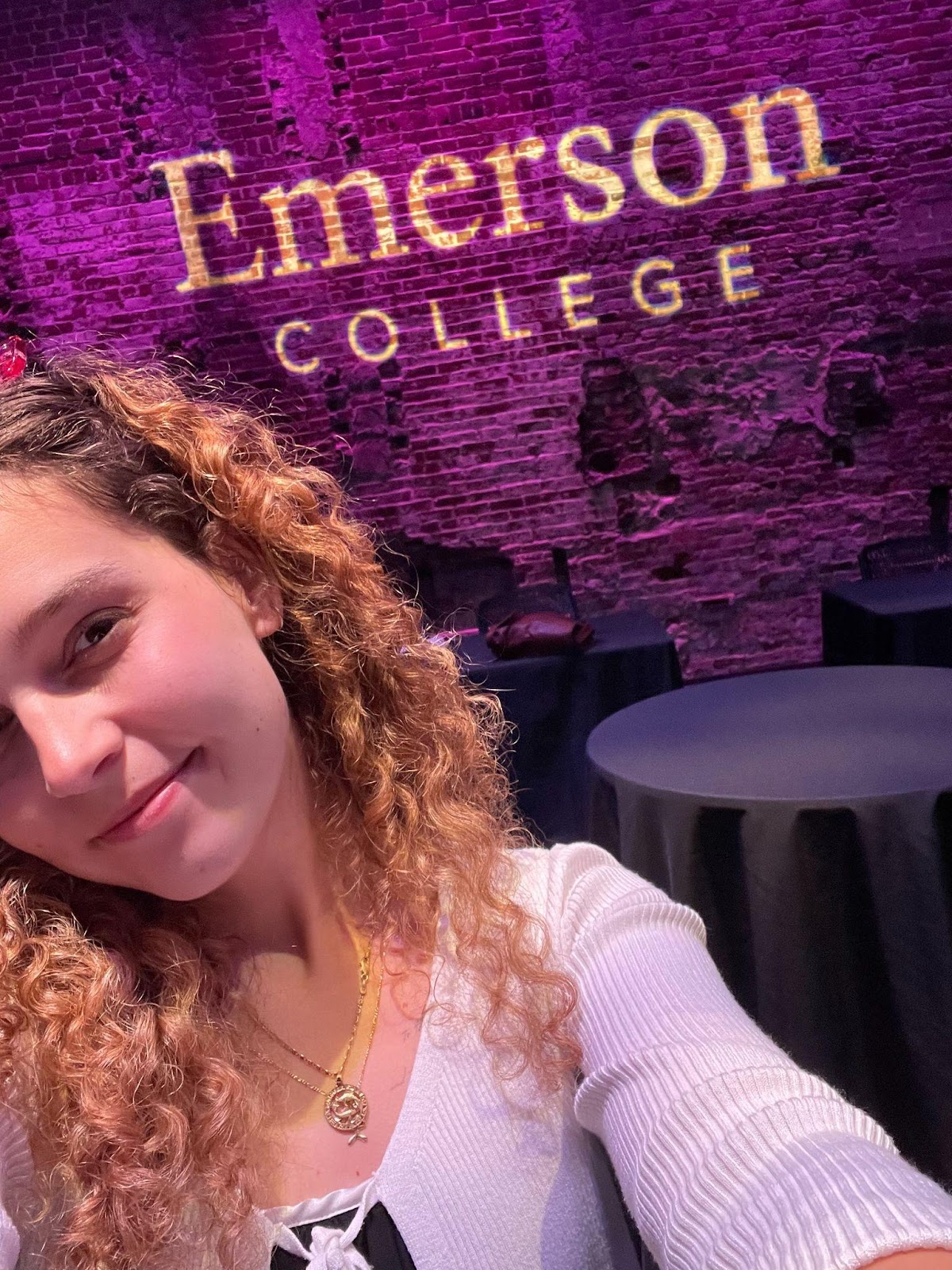 Selfie of Robin Van Impe in in front of Emerson College's logo projected on a brick wall.