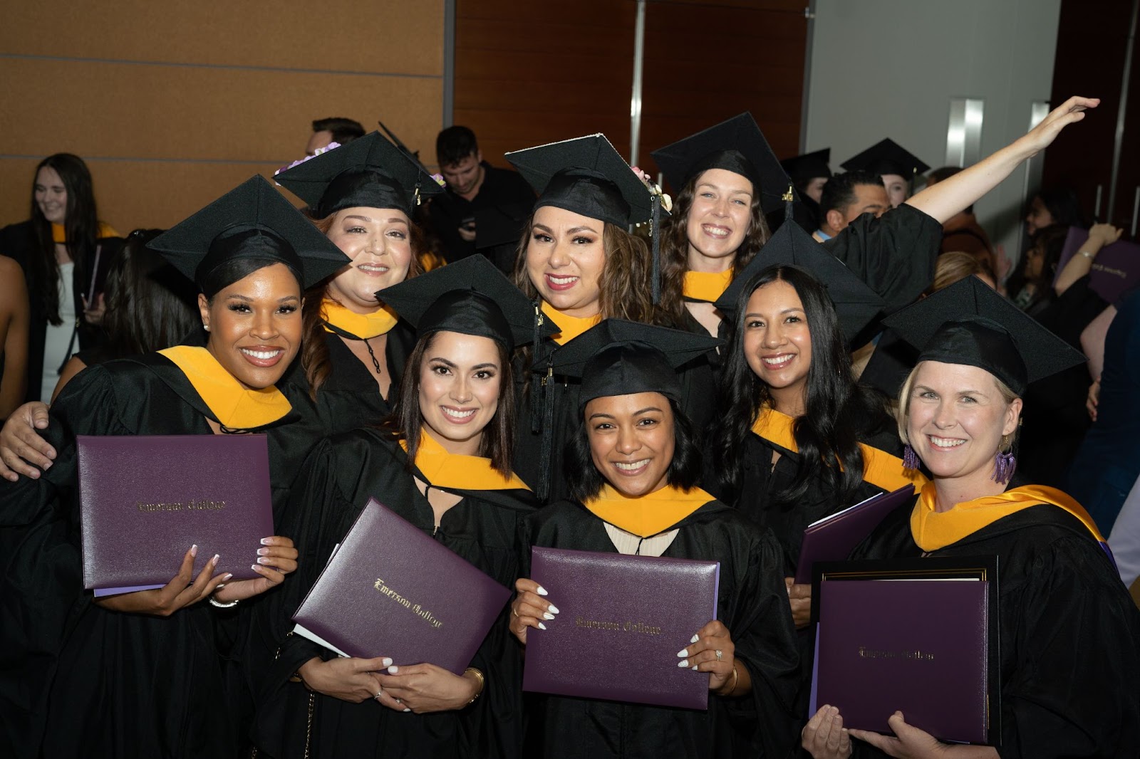 Group of graduates smile broadly at the camera while holding their diplomas. 