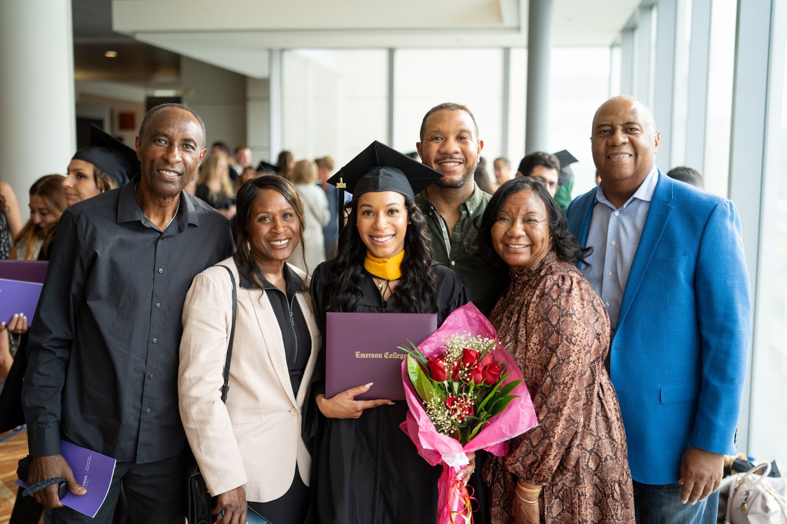 A family smiles broadly at the camera as the graduate holds her diploma and bouqet of roses.