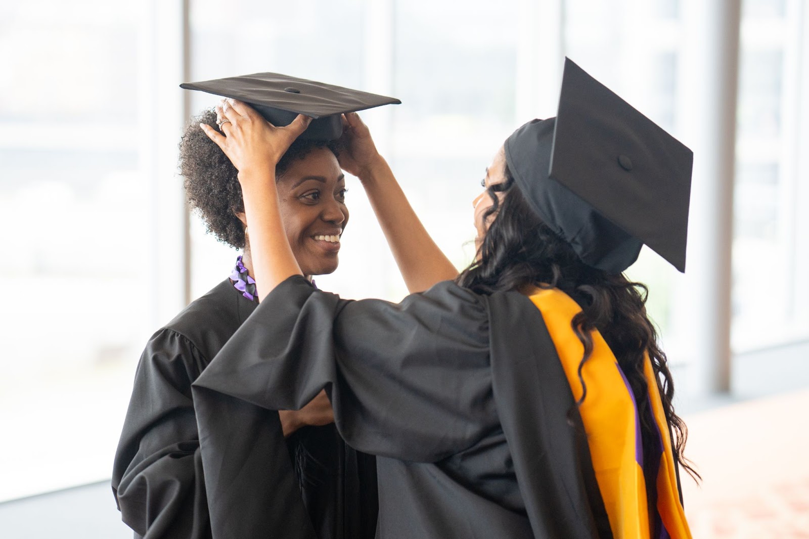 One graduate adjusts the cap of another graduate to sit straight.