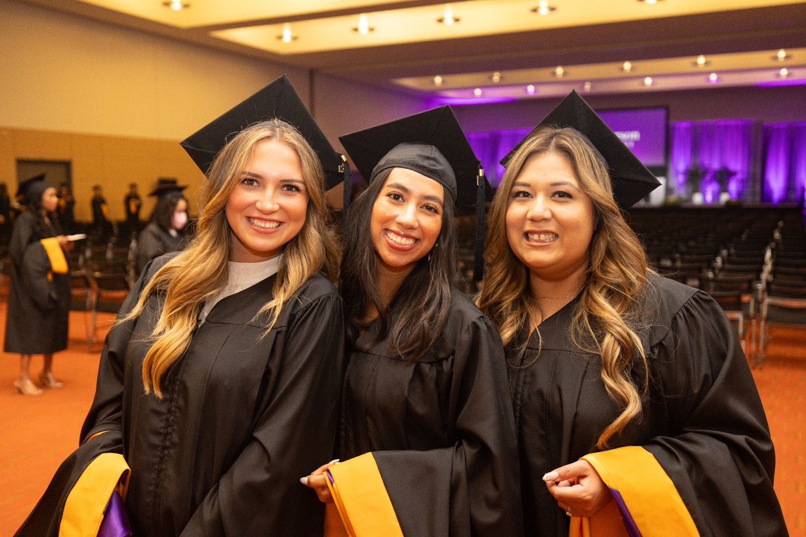 Three female graduates smile at the camera enthusiastically. 