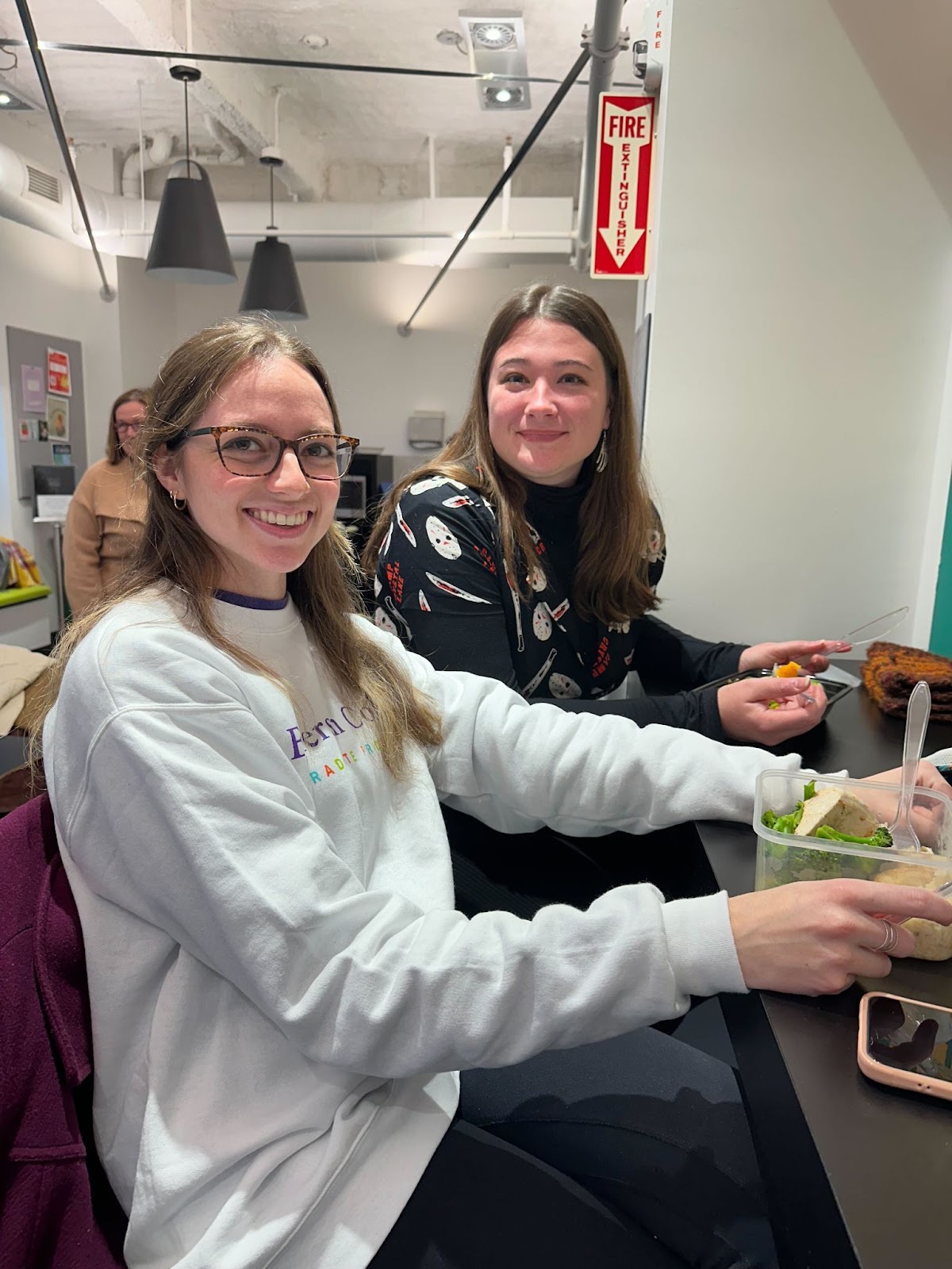 Two students smile at the camera with meal preps in front of them.