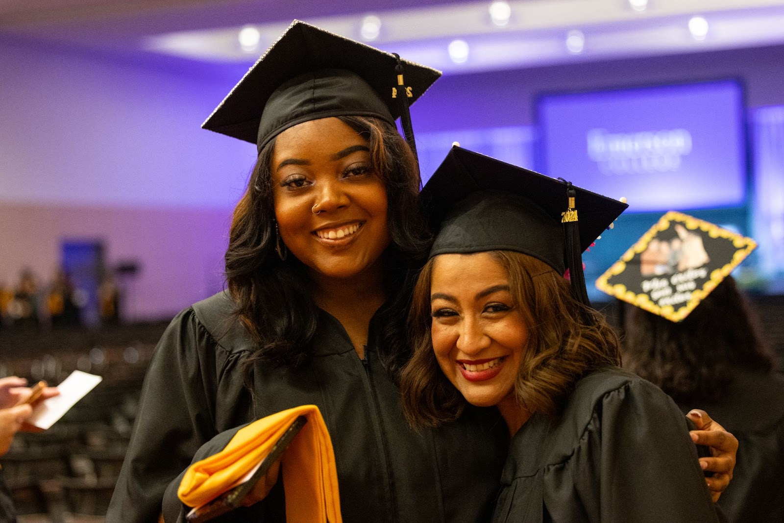 Two graduates embrace with smiles.