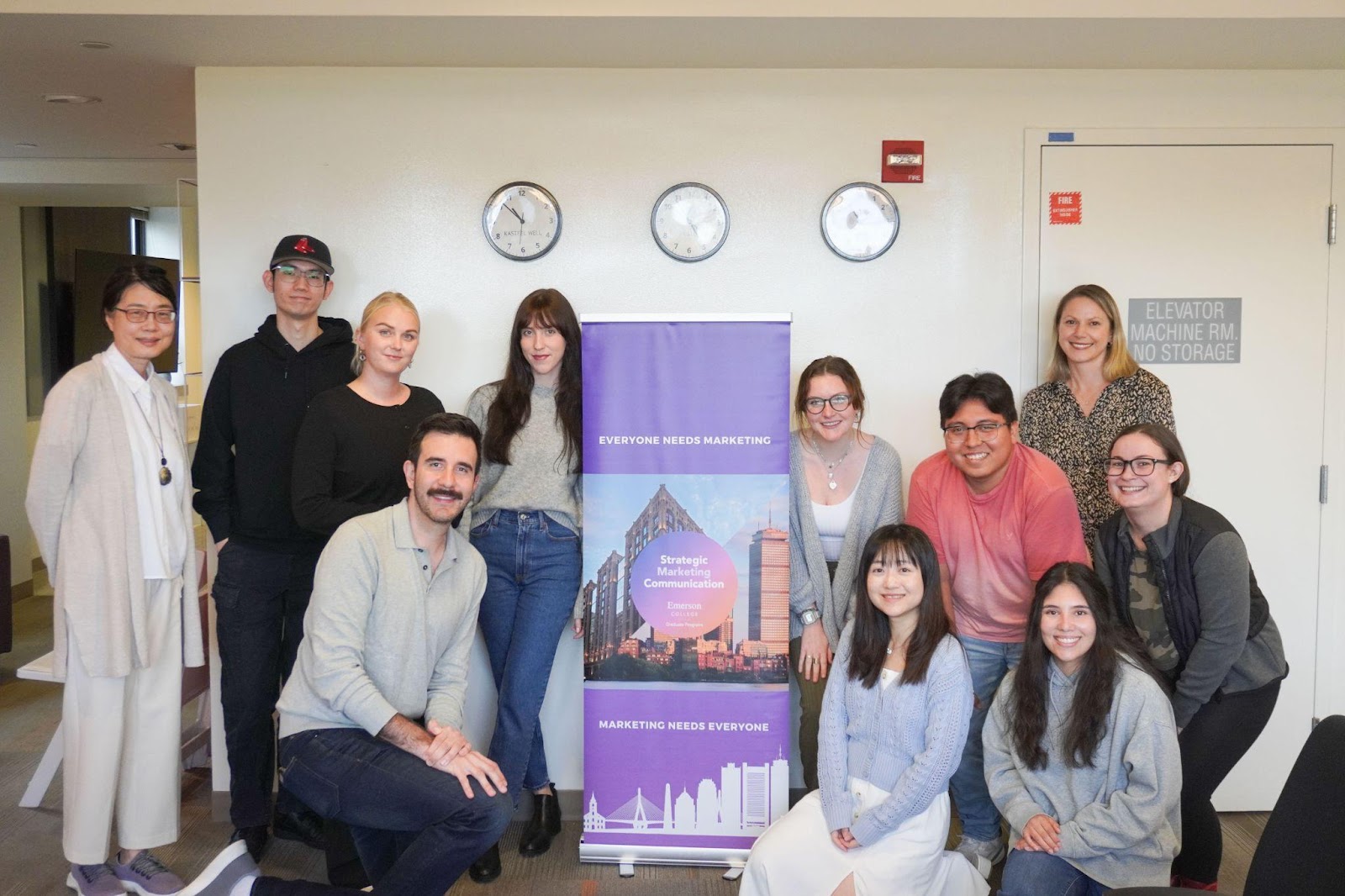 The Strategic Marketing and Communications cohort smiles together in front of a sign for their program.