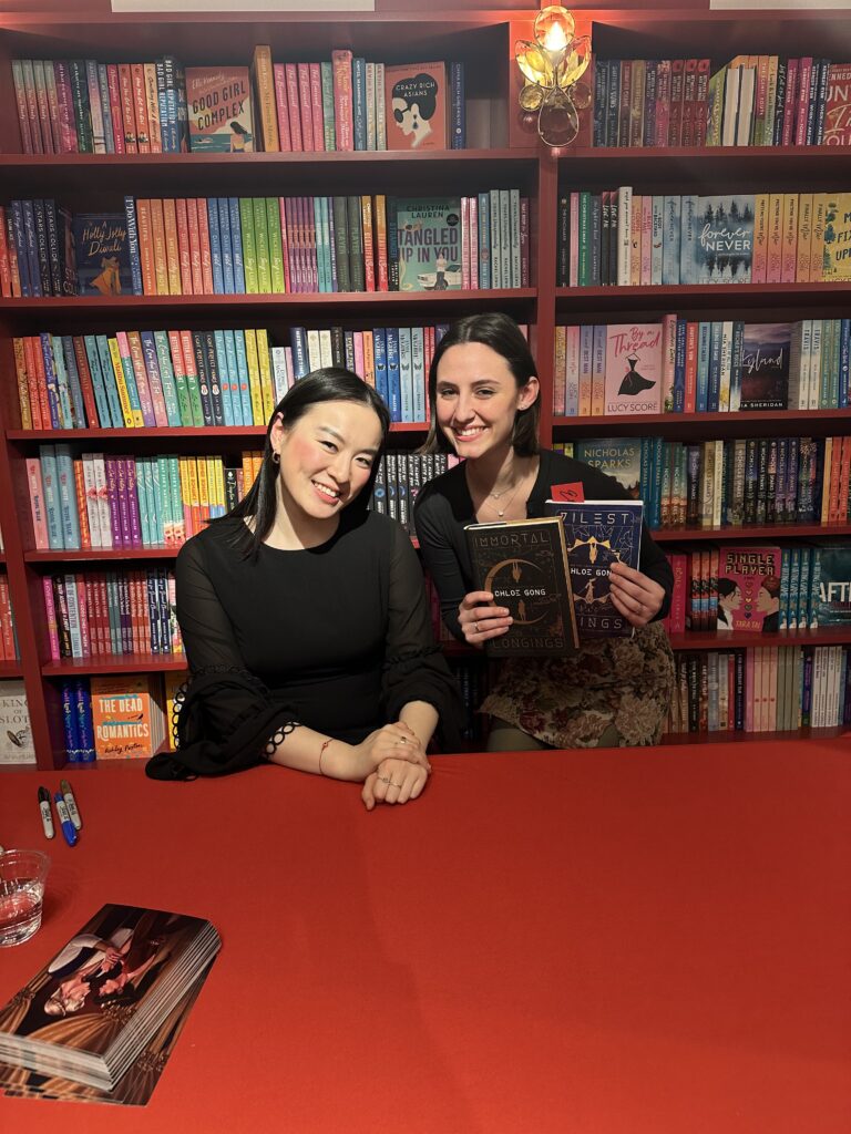 Emily smiling beside romance author Chloe Gong while holding two of Chloe's recently published books.