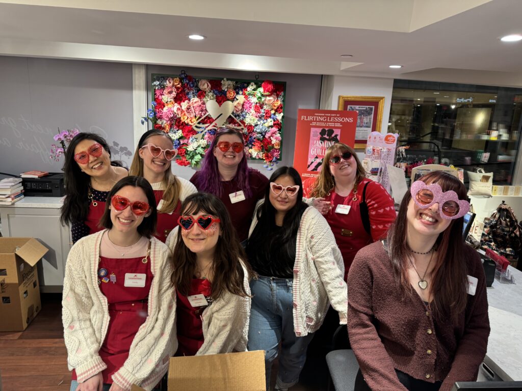 Members of the Lovestruck Books staff smiling at the camera with heart-shaped sunglasses for Valentine's Day.