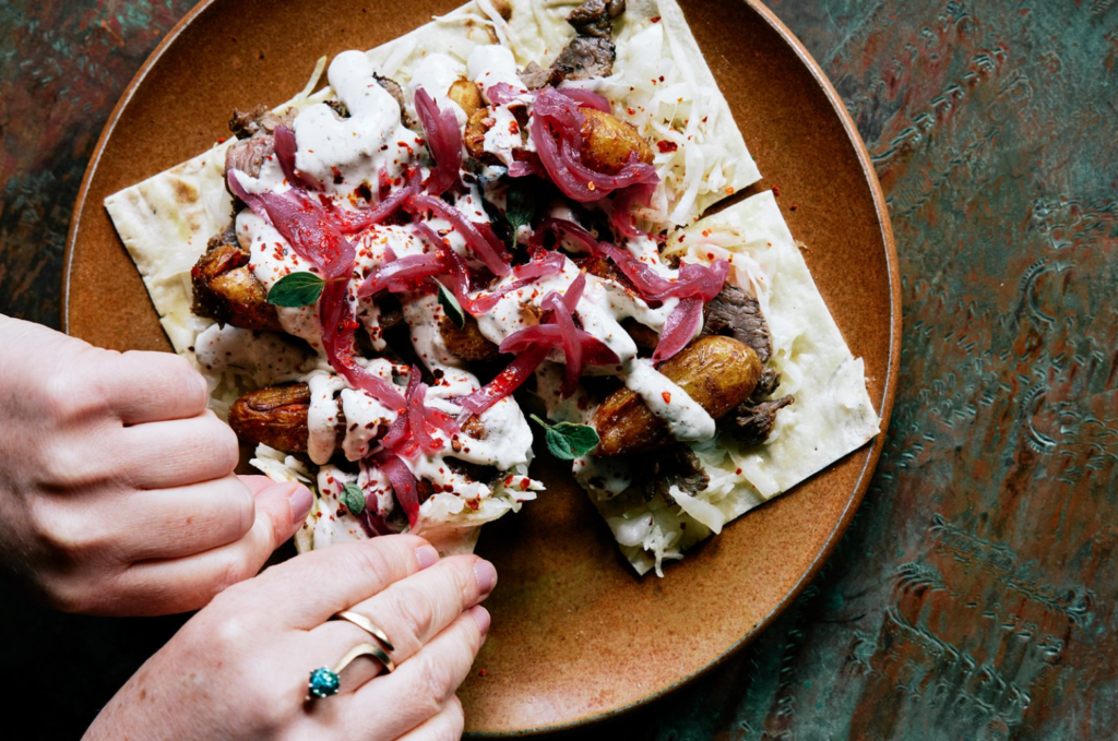 Flatbread topped with potatoes, steak, pickled onions, and a tzatziki sauce. 