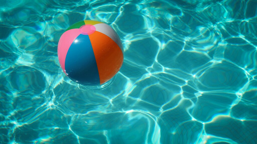 A multi-colored beach ball floats in the pool water on a sunny day.