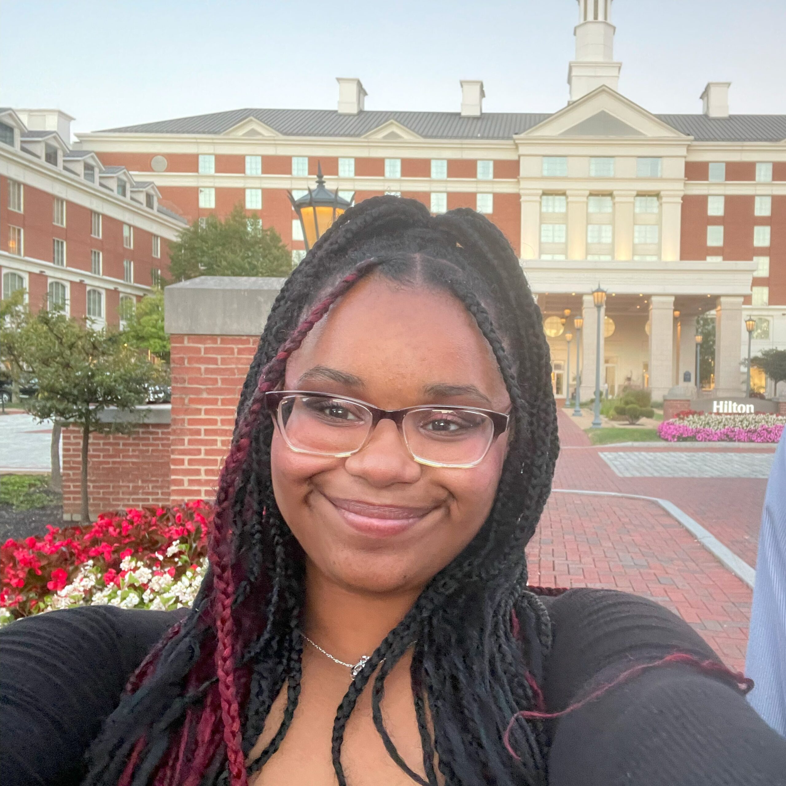 A selfie of Aniaha. She is a Black woman with glasses, braids in her hair, and is wearing a black shirt.