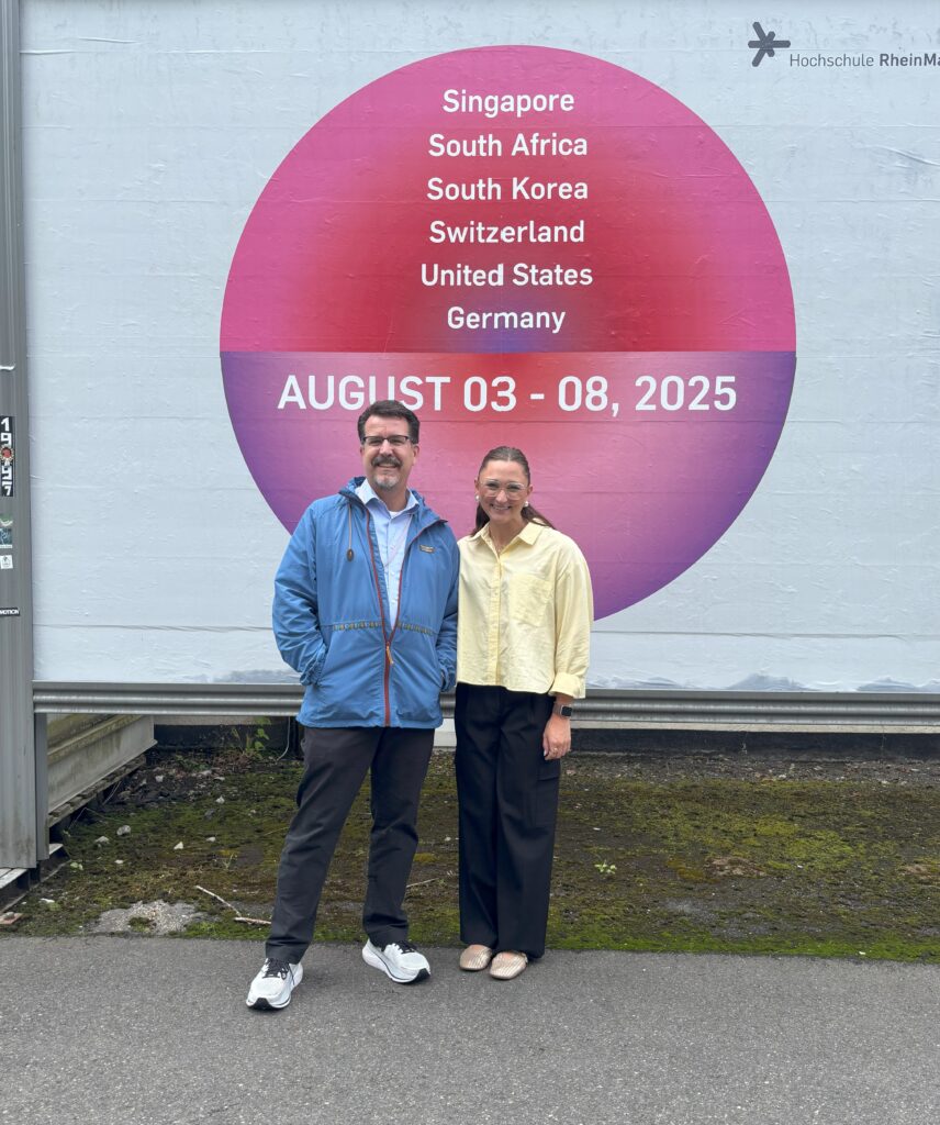 Jillian stands with her professor in front of an outdoor mural that advertises the five-day international marketing trip. 