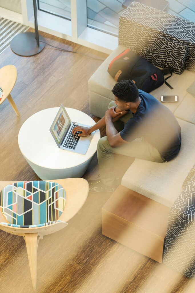 A Black man sits at a white table with his computer open.