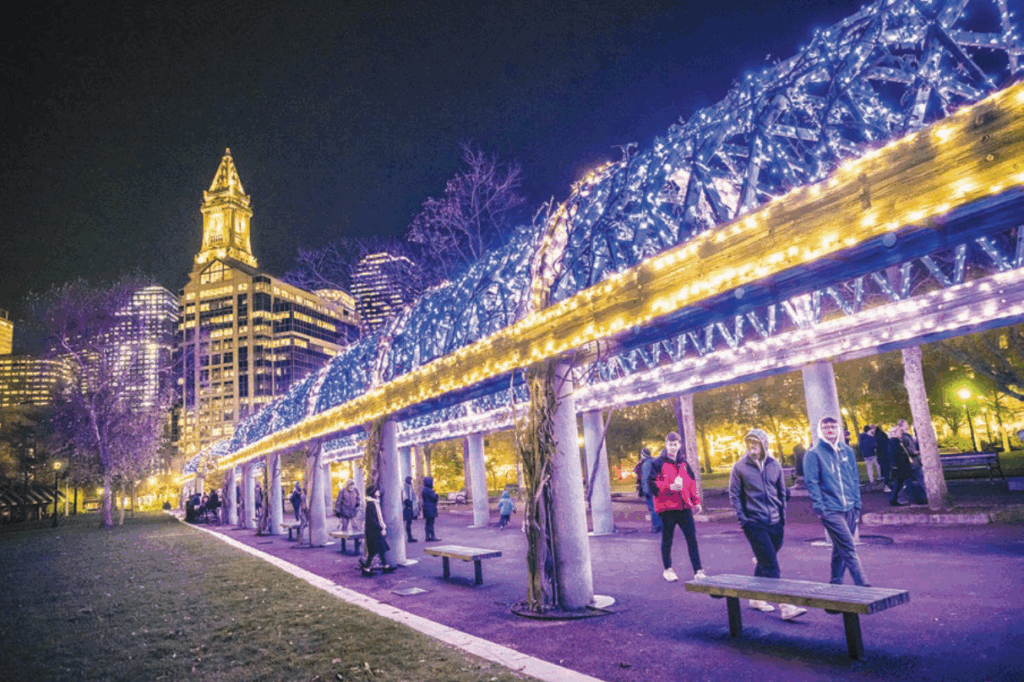 Trellis at Christopher Columbus Park lit up with blue and gold lights, with the city skyline in the background.