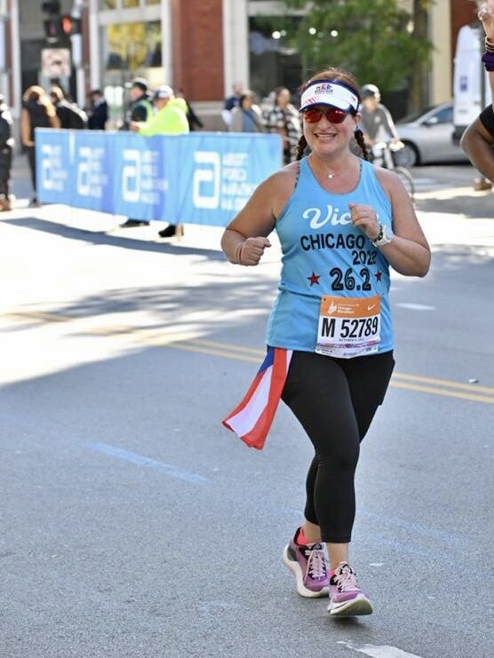 Dr. Bou running the Chicago Marathon wearing a bright blue shirt, white visor, and sunglasses.