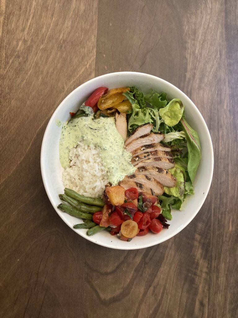 Chicken and rice in a white bowl with lettuce, tomatoes, and green beans.