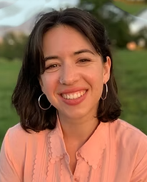 Tamar smiles at the camera. She is wearing a pink blouse, has brown shoulder-length hair, and silver hoop earrings.