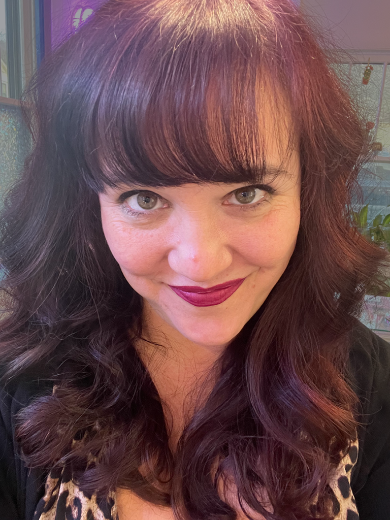 Selfie of Mickie, with burgundy hair and a soft smile.