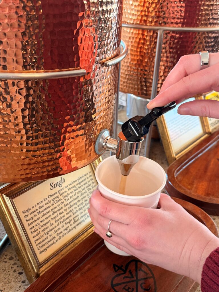 A white hand is pouring tea into a cup from a copper thermos.