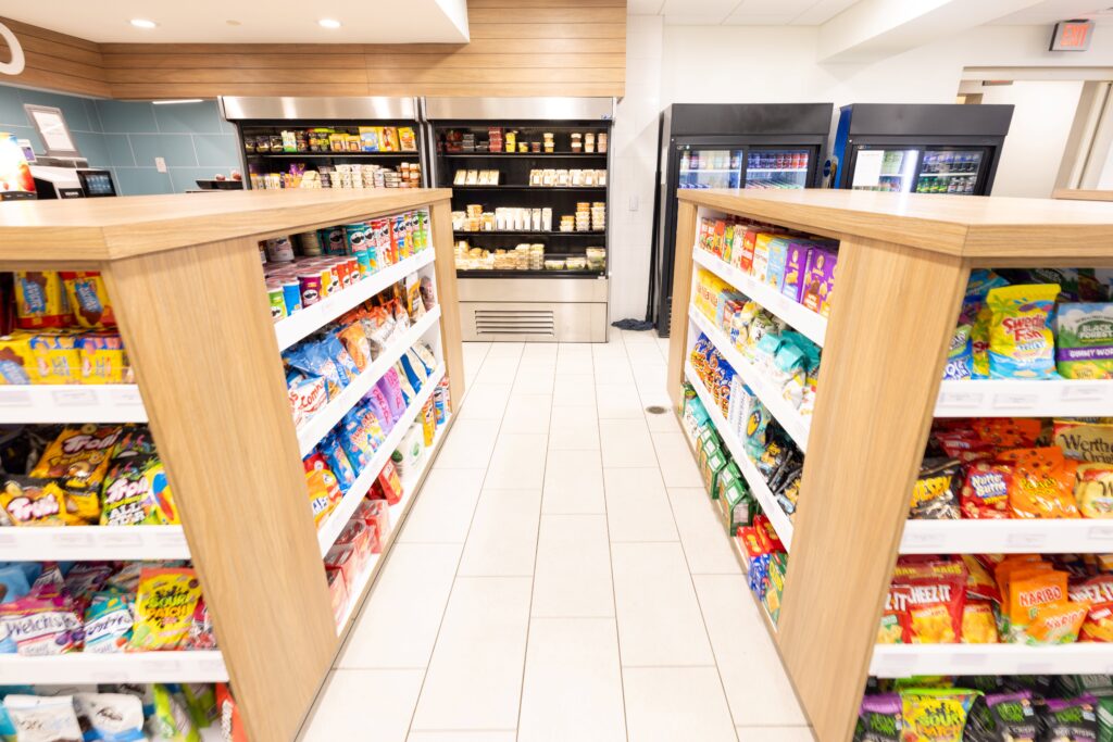 Two stand-alone shelves hold a large array of colorful packaged goods, while fridges in the back have drinks and grab-and-go items.