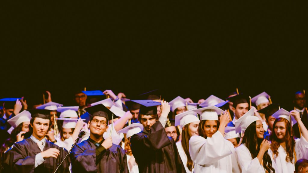 Students stand on a stage in black and white graduation cap and gowns.