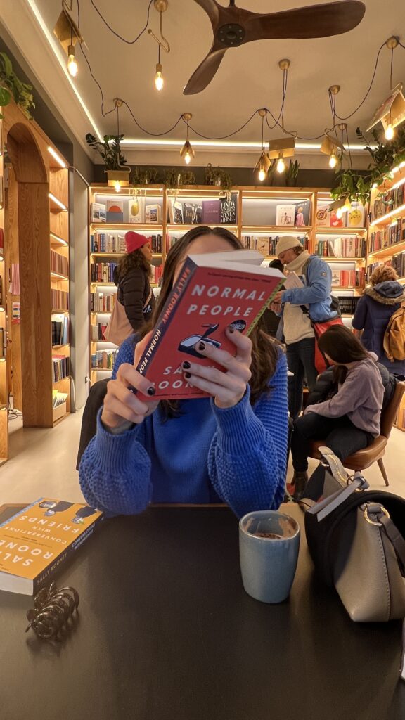 Girl in blue sweater is holding "Normal People" book by Sally Rooney.