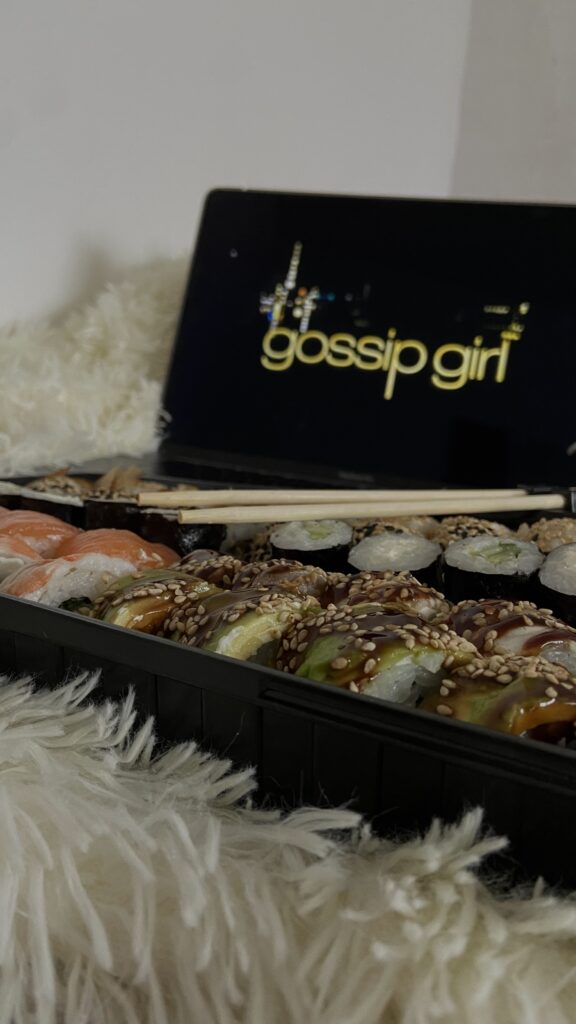 Computer screen shows "gossip girl" with a plate of sushi in front of the computer.