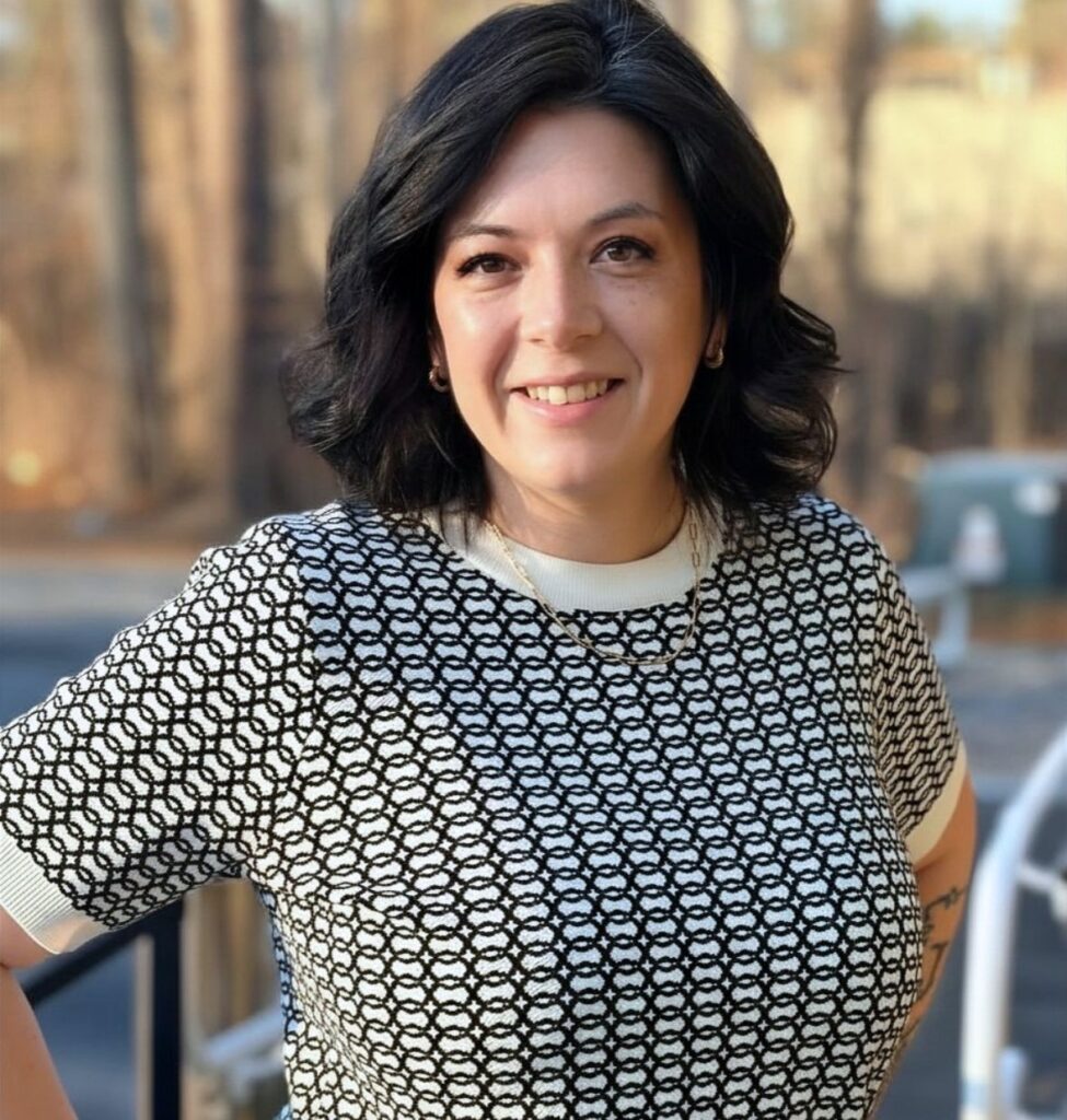 close up of woman smiling. She has pale skin and black hair. She is wearing a black and white check sweater