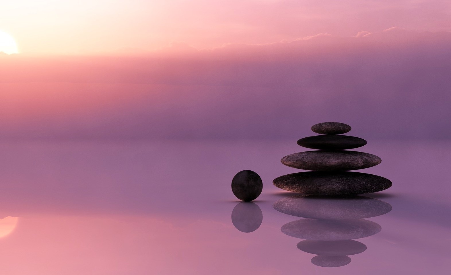 A pile of stones in front of pink, serene water.