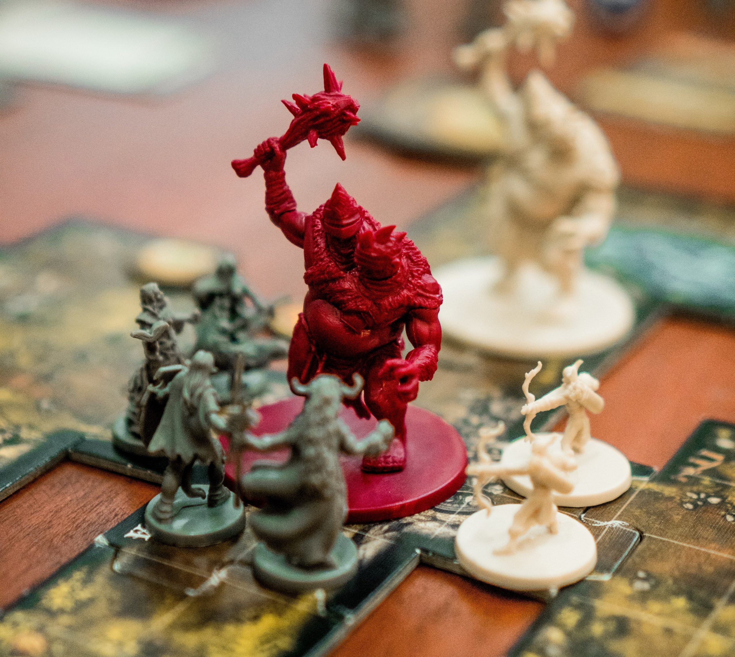 A gameboard on which a group of small adventurer figures confronts a large red troll figure.