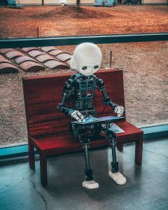 Photograph of a robot sitting on a bench reading a pamphlet 
