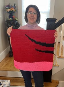 Liz Chase holding a red and pink crochet square