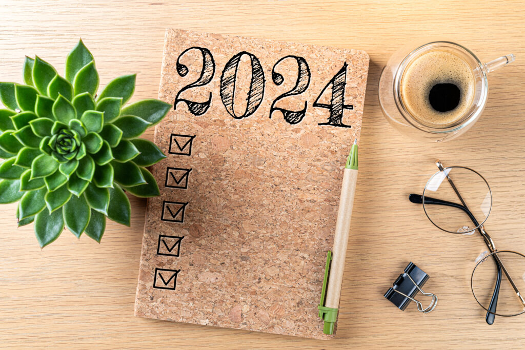 New year resolutions 2024 on desk. 2024 goals list with notebook, coffee cup, plant on wooden table. 