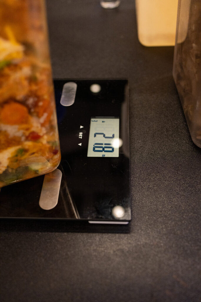 Up close image of edible food waste in clear bin being weighed on a scale.