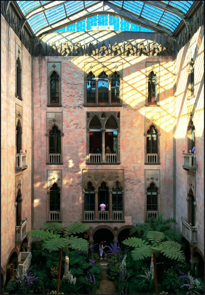 A picture of the Gardner Museum courtyard from the second floor. The camera overlooks the sun roof as afternoon light casts a bright yellow cast on the pink brick walls above the courtyard plants.